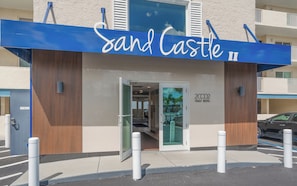 A hotel entrance with a blue awning and a sign that reads 'Sand Castle II'. - New Direct Beachfront 3/2 Upscale, Beachfront Condo, Recliners, Pool, Hot Tub (Indian Rocks Beach)