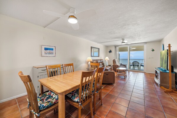 A dining area with a wooden table and chairs, a ceiling fan, and a view of the ocean through a sliding glass door. - New Direct Beachfront 3/2 Upscale, Beachfront Condo, Recliners, Pool, Hot Tub (Indian Rocks Beach)