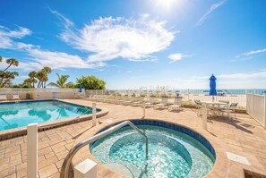 A pool area with a hot tub, lounge chairs, and a view of the beach. - New Direct Beachfront 3/2 Upscale, Beachfront Condo, Recliners, Pool, Hot Tub (Indian Rocks Beach)