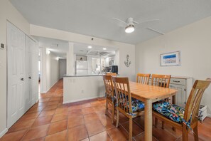 A dining area with a wooden table and chairs, a ceiling fan, and a kitchen in the background. - New Direct Beachfront 3/2 Upscale, Beachfront Condo, Recliners, Pool, Hot Tub (Indian Rocks Beach)