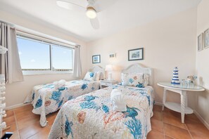 A hotel room with two beds, a ceiling fan, a window with curtains, a small table with a lamp, and a wall with framed pictures. - New Direct Beachfront 3/2 Upscale, Beachfront Condo, Recliners, Pool, Hot Tub (Indian Rocks Beach)