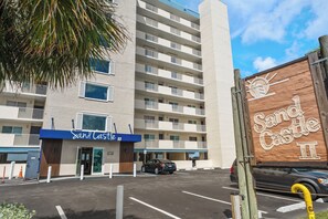 A multi-story hotel with a sign reading 'Sand Castle II' and a parking lot in front. - New Direct Beachfront 3/2 Upscale, Beachfront Condo, Recliners, Pool, Hot Tub (Indian Rocks Beach)