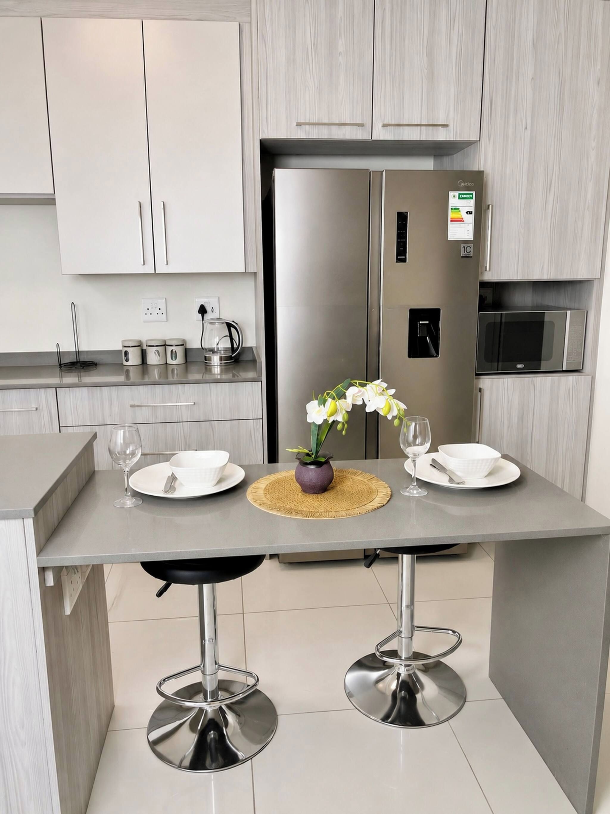 Cozinha moderna com geladeira embutida, micro-ondas e mesa de jantar com dois banquetes.