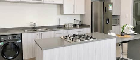 Una cocina moderna con una isla central, electrodomésticos de acero inoxidable y lavadora integrada.