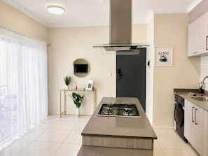 A modern kitchen with a central island, a built-in stove, and a stainless steel range hood. - Luxury 1BR Suite at 92 on New (Johannesburg)