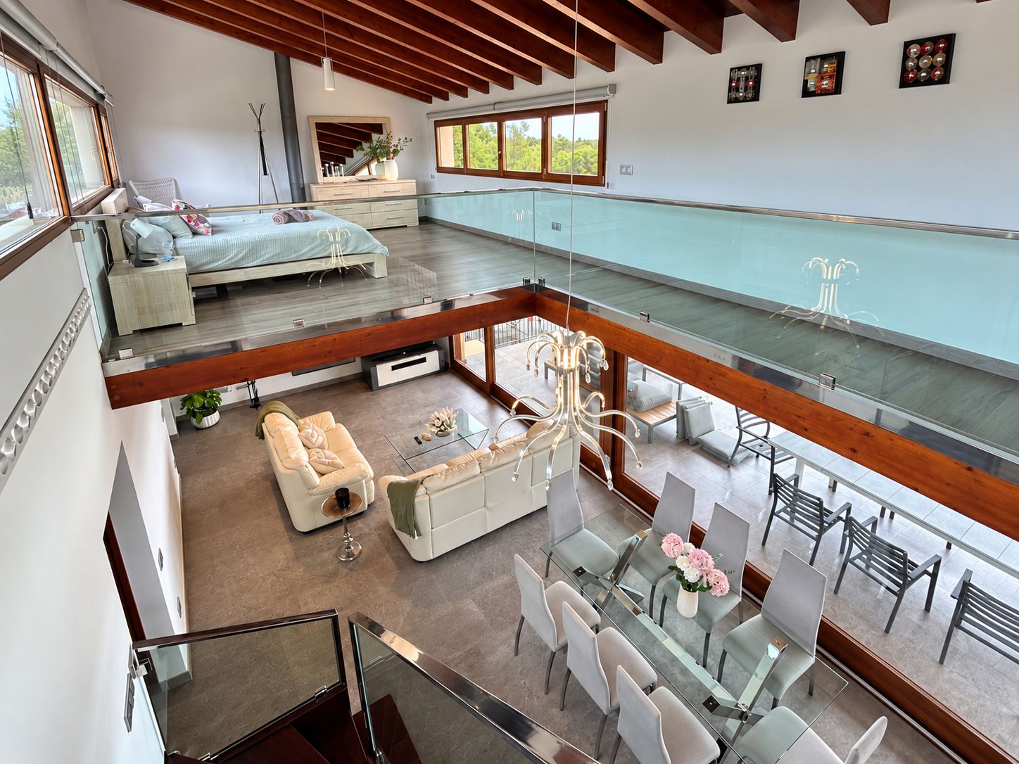 Un vaste espace de vie aménagé dans un style loft, avec un plafond haut, un coin repas doté de tables en verre et un balcon offrant une vue dégagée.