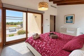 A bedroom with a large bed, a view to the outside, a crib, and a painting on the wall. - Can Maimó Estate (Santanyí)