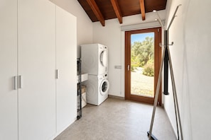 A laundry room with stacked washing machines, a drying rack, and a door leading outside. - Can Maimó Estate (Santanyí)
