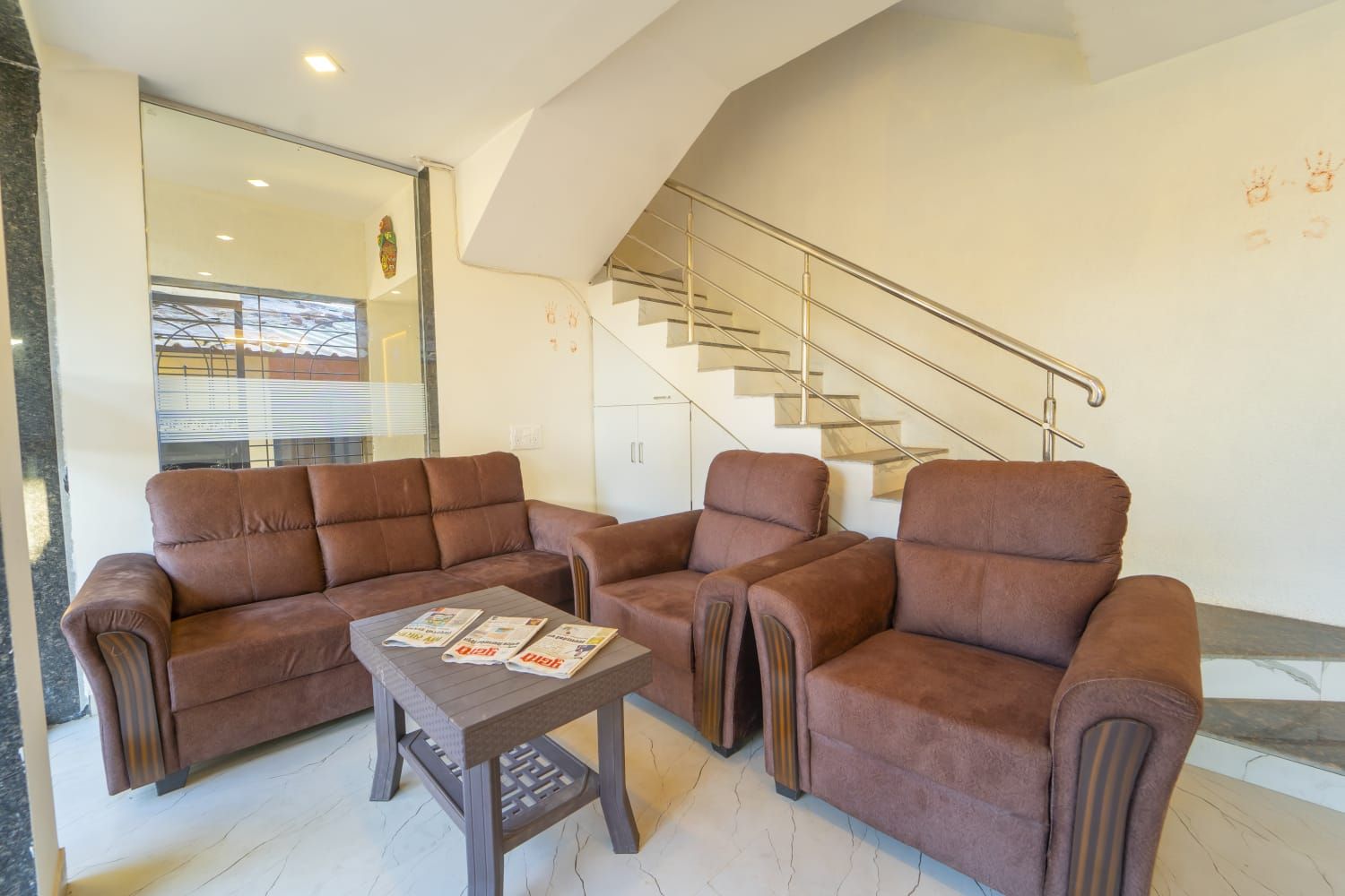 Una sala de estar moderna con un conjunto de sofás, una mesita de centro con periódicos y una escalera.