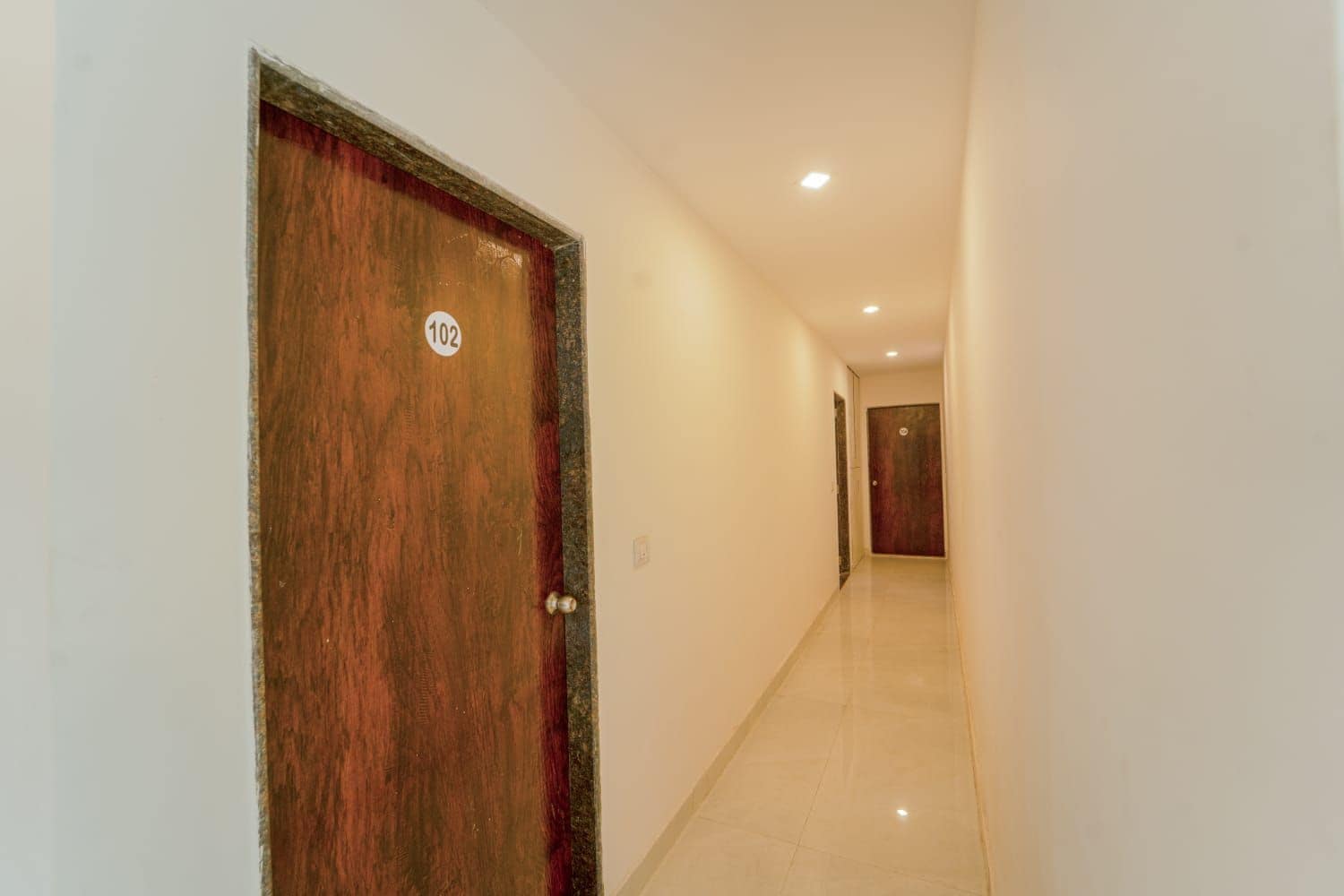 Un pasillo con una puerta de madera marcada con el número 102, que conduce a otra puerta al final.