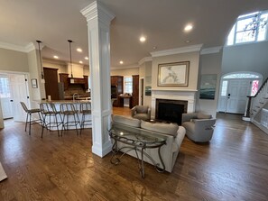 A spacious living area with a fireplace, a dining area with bar stools, and a kitchen in the background. - Private 15-Acre River Estate • Sleeps 14 (New Hill)