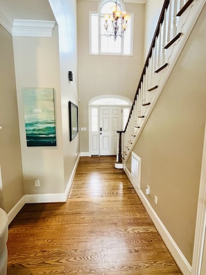 A hallway with a wooden floor, a chandelier, a framed picture, and a white door at the end. - Private 15-Acre River Estate • Sleeps 14 (New Hill)
