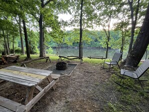 A campsite with a picnic table, chairs, and a fire pit. - Private 15-Acre River Estate • Sleeps 14 (New Hill)
