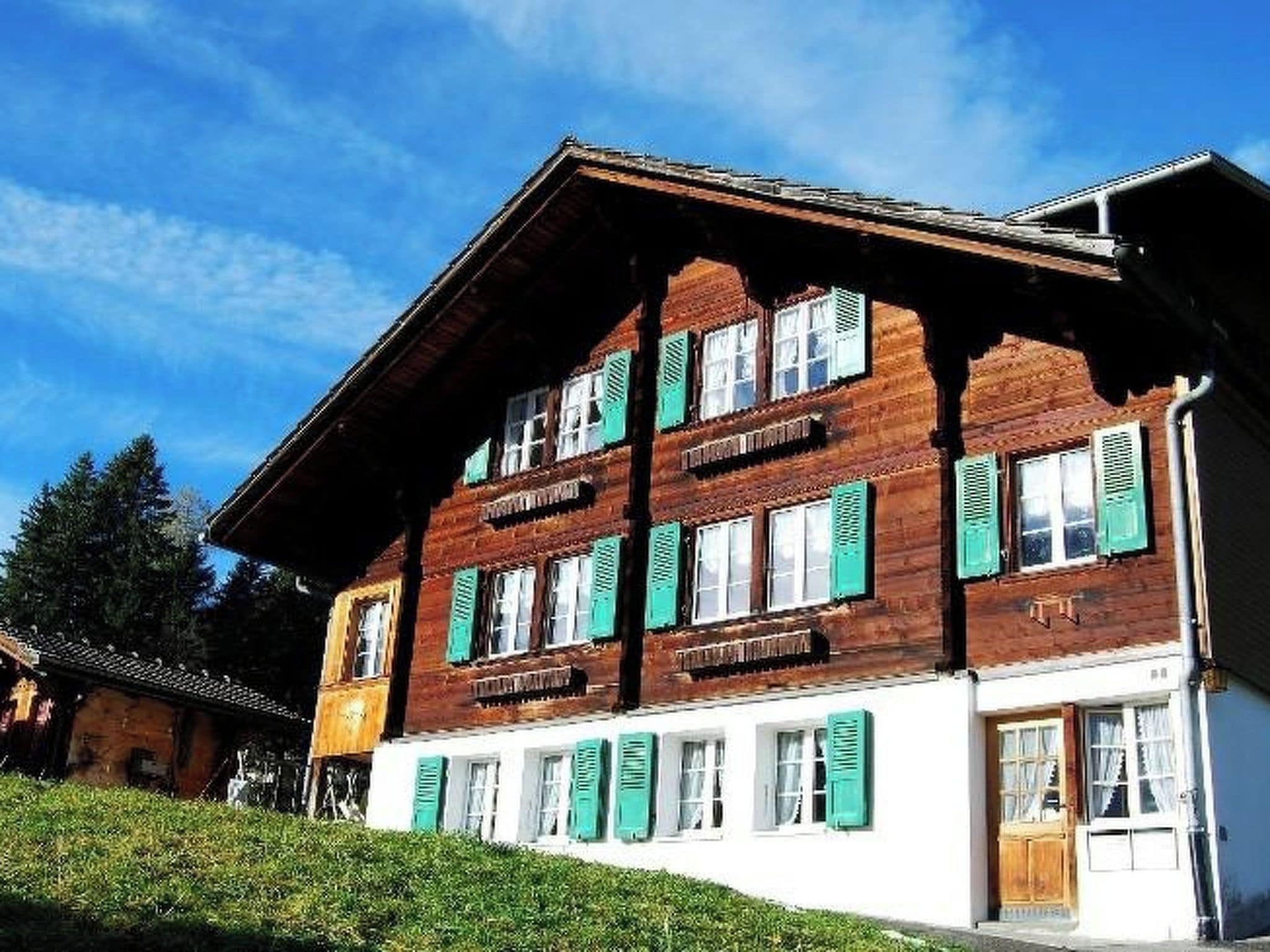 A two-story wooden building with multiple windows and shutters, a sloped roof, and a well-maintained lawn.