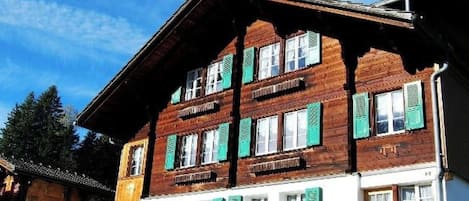 Un bâtiment en bois à deux étages, doté de nombreuses fenêtres et volets, d’un toit en pente et d’une pelouse bien entretenue.