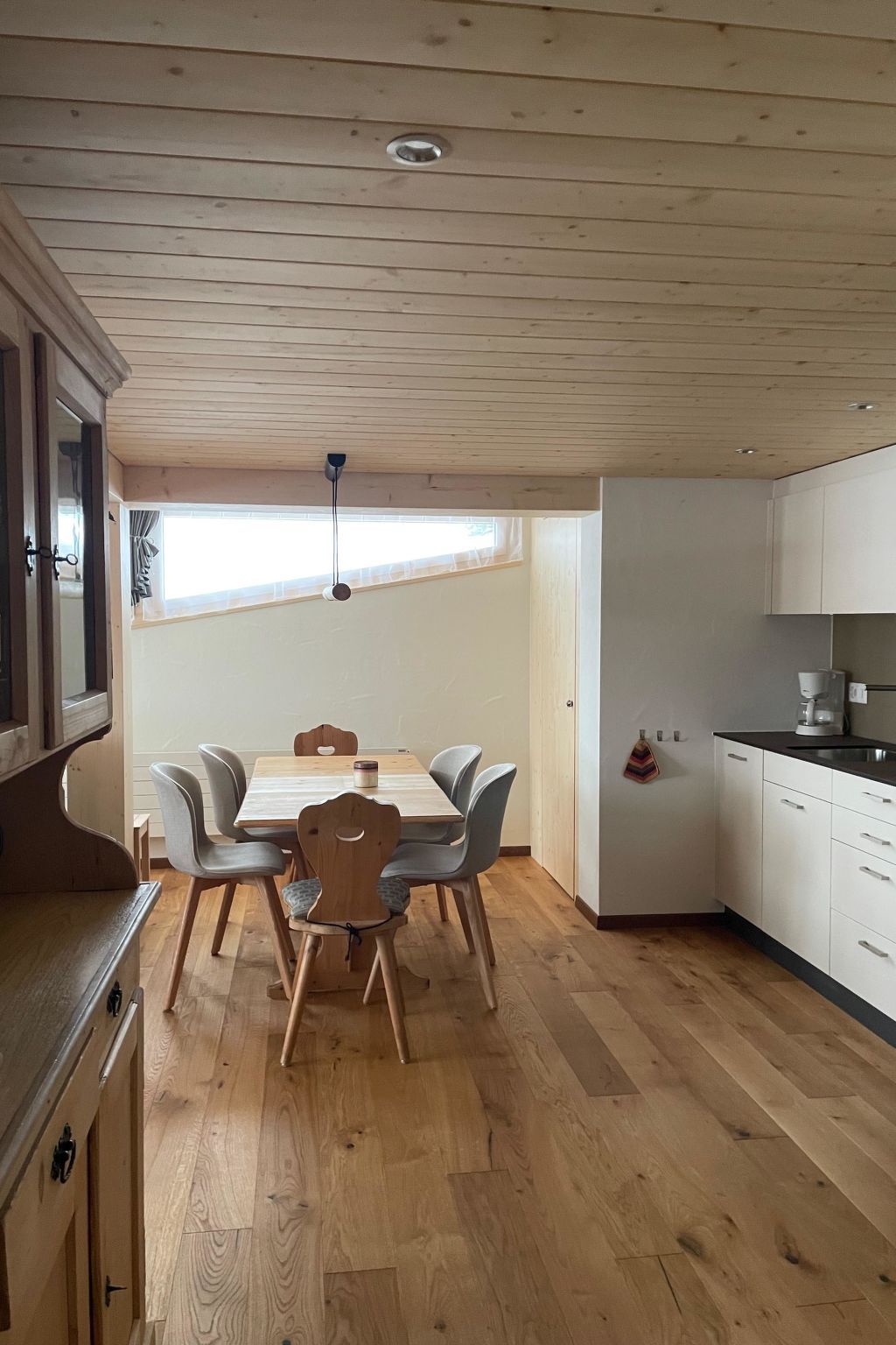 A modern kitchen with wooden flooring, a dining area with a table and chairs, and a built-in oven.