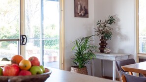 Ein Essbereich mit Tisch, Stühlen, einer Fruchtschale, einer Topfpflanze und einer Blumenvase.