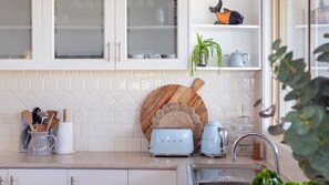 Eine Küche mit weißen Schränken, einem Holztisch zum Schneiden und einer Abteilung für Küchengeräte, einschließlich Toaster und Wasserkocher.