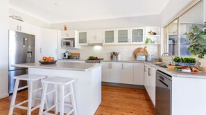 Eine moderne Küche mit weißen Schränken, einem Edelstahl-Kühlschrank, einer Mikrowelle und einer Holztheke mit Hockern.