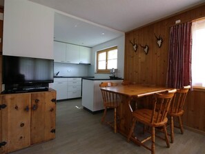 Cozinha compacta com área de refeições, armários de madeira e uma televisão em um móvel.