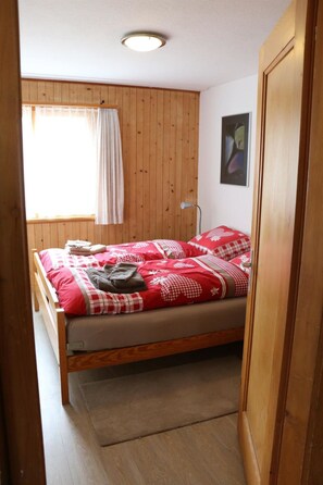 Ein kleines Zimmer mit einem Einzelbett, Holzwänden und einer Deckenleuchte.