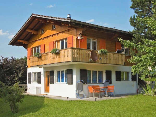 Ein zweistöckiges Holzhaus mit einem Balkon, einem Essbereich mit Gartenmöbeln und einem gepflegten Rasen.