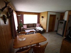 Interior acolhedor de uma cabana com uma mesa de jantar de madeira, um sofá e uma geladeira.
