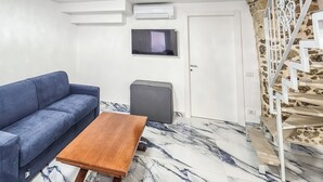 Ein Zimmer mit einer Couch, einem kleinen Tisch, einem Fernseher und einer Treppe.