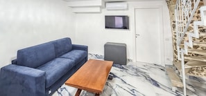 A room with a sofa, a small table, a television, and a staircase. - Monte Bello Suites (Montescaglioso)