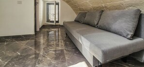 Un pasillo con piso de mármol que conduce a una habitación con un sofá gris y una pared de piedra.