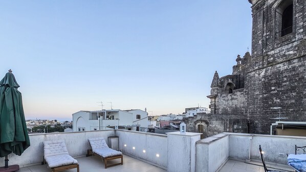 Terraza en la azotea con sillones de descanso y una sombrilla verde, con vistas a un edificio histórico y al paisaje urbano.