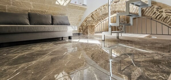 A modern interior with a sofa, a polished marble floor, and a stone wall.