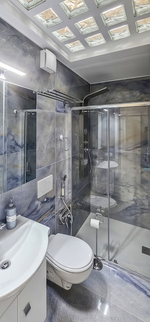 A modern bathroom with a glass shower enclosure, a white toilet, and a marble-tiled vanity. - Monte Bello Suites (Montescaglioso)