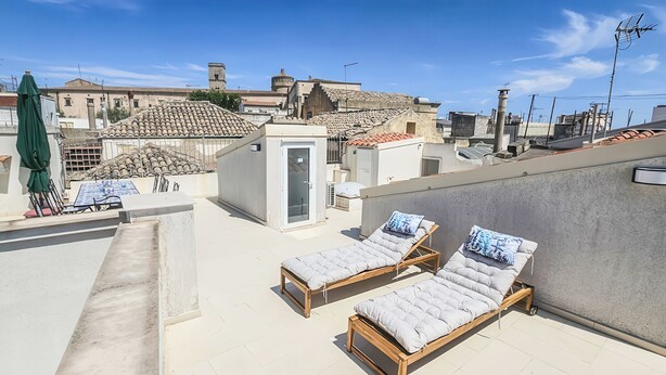 Eine Dachterrasse mit zwei Liegestühlen, einem kleinen Tisch und einem grünen Sonnenschirm.