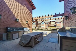 An outdoor patio area with barbecue grills, a covered table, and a pergola structure. - Stylish, fully equipped 2-bed / 2-bath condo in Riverstone Village, Coeur d'Alene, with open floor plan, fully equipped kitchen, and secure garage parking. Walkable to nearby dining, shopping, trails, parks and the waterfront. (Coeur d'Alene)