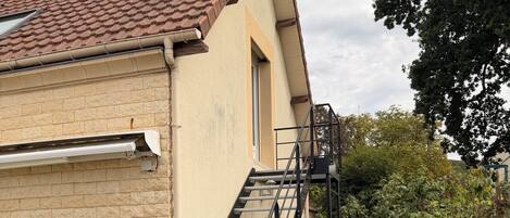 A building with a tiled roof, a staircase, and a concrete pathway leading to a door.