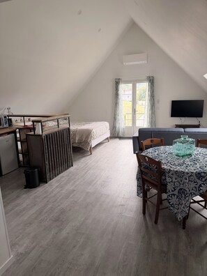 A room with a bed, a dining table with chairs, a TV, and a window with curtains.