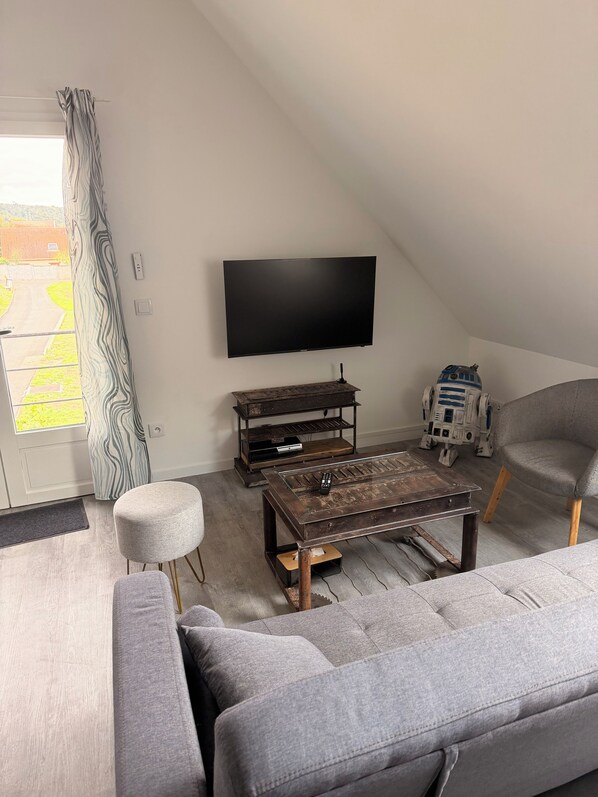 A living room with a flat-screen TV, a Star Wars R2-D2 figure, a grey sofa, and a coffee table.