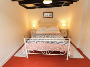 Ein Bett mit Metallgestell, zwei Nachttische mit Lampen, ein gerahmtes Bild über dem Bett und ein roter Boden.