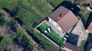 Eine Vogelperspektive auf ein Anwesen mit einem Ziegeldach, einem eingezäunten Grünbereich und Steinmauern.