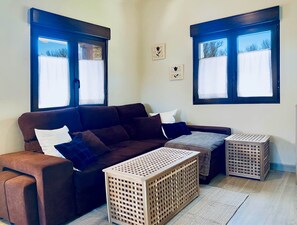 Ein Wohnzimmer mit einem braunen Sofa, zwei Holzkisten und einem Fenster mit Blick auf Bäume.