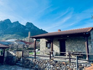 Un bâtiment en pierre avec un toit en tuiles, un mur en pierre et une vue sur les montagnes en arrière-plan.