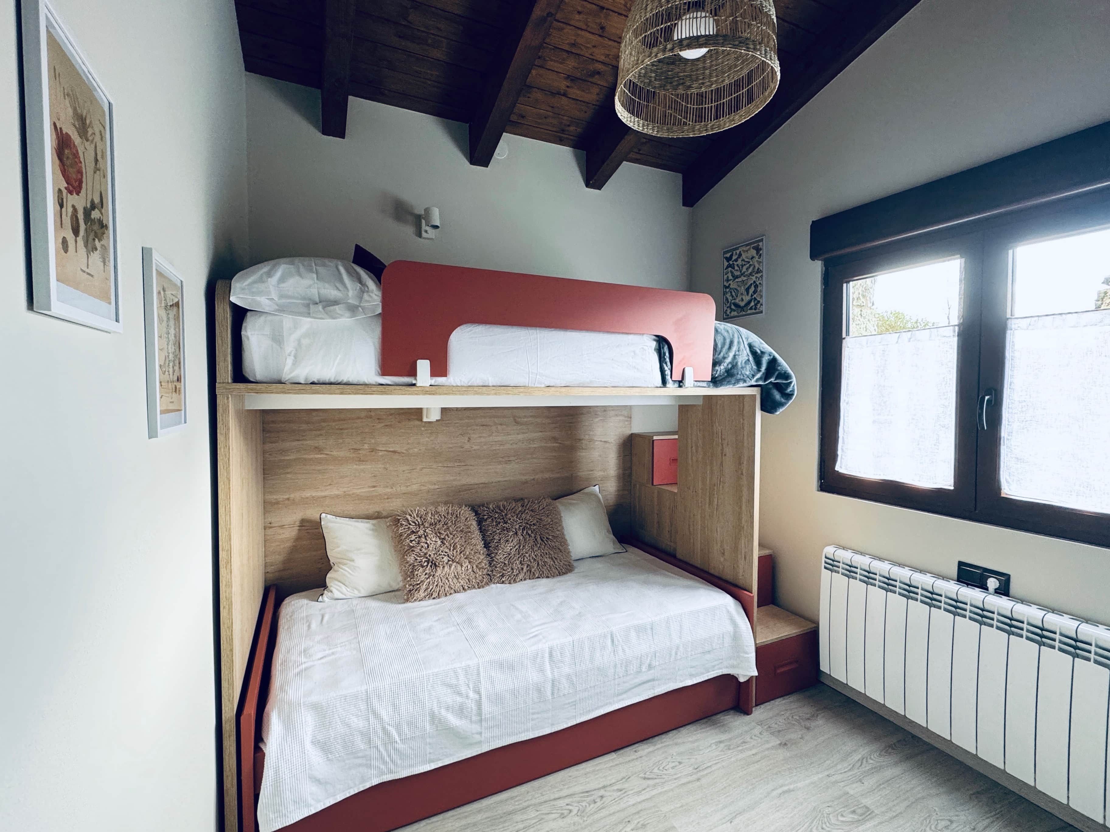 Un lit superposé avec un lit en bas et un lit en haut, une fenêtre avec des stores, un radiateur et un luminaire au plafond.