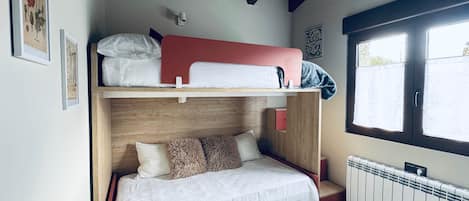 Un lit superposé avec un lit en bas et un lit en haut, une fenêtre avec des stores, un radiateur et un luminaire au plafond.