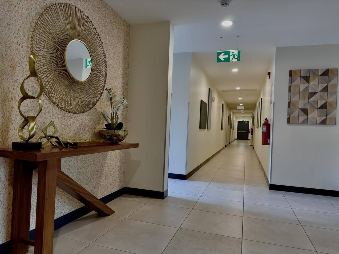 Un pasillo de hotel con un espejo, una planta y una obra de arte geométrica en la pared.