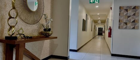 Un couloir d’hôtel avec un miroir, une plante et une œuvre d’art géométrique accrochée au mur.