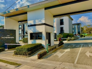 A modern hotel entrance with a clear sky, a sign reading 'NOVATRIANA,' and a parking area with directional arrows. - Best place near the airport SJO with Air Cond (Alajuela)
