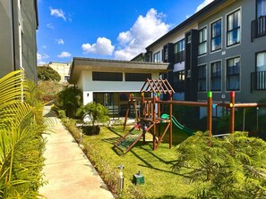 A playground with a slide and climbing structures, surrounded by a well-maintained lawn and a building with large windows. - Best place near the airport SJO with Air Cond (Alajuela)