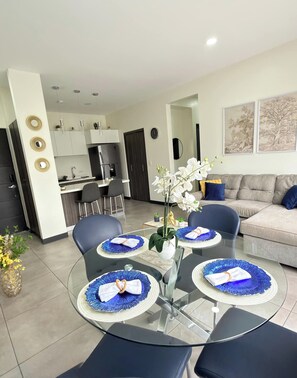 A modern living room with a glass dining table, blue chairs, and a sofa with cushions. - Best place near the airport SJO with Air Cond (Alajuela)