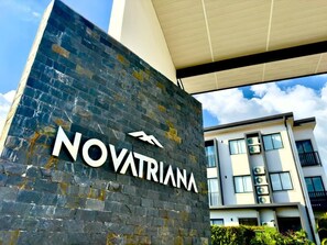 A building with a sign reading 'NOVATRIANA' and a modern architectural style with a flat roof and large windows. - Best place near the airport SJO with Air Cond (Alajuela)